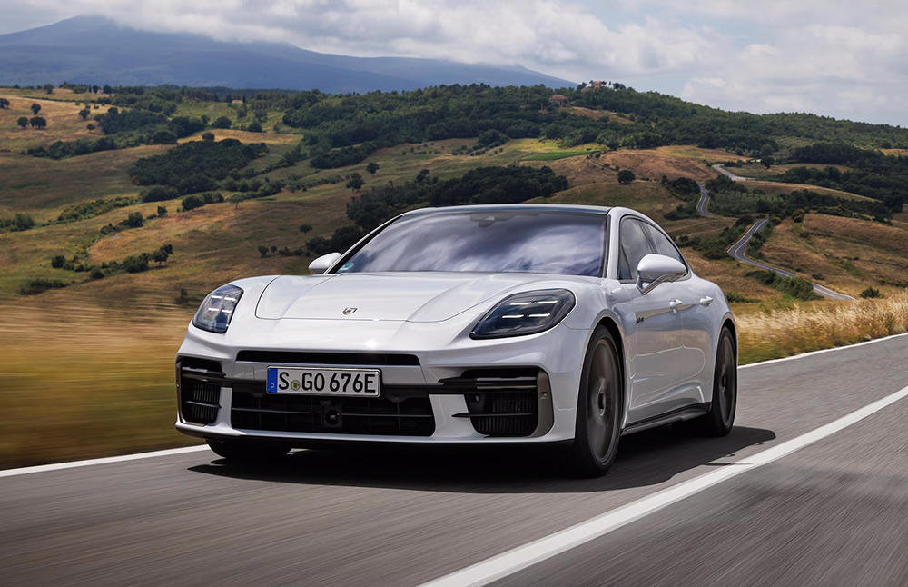 Front photo of a white porsche panamera turbo driving on the road, with a background of a field